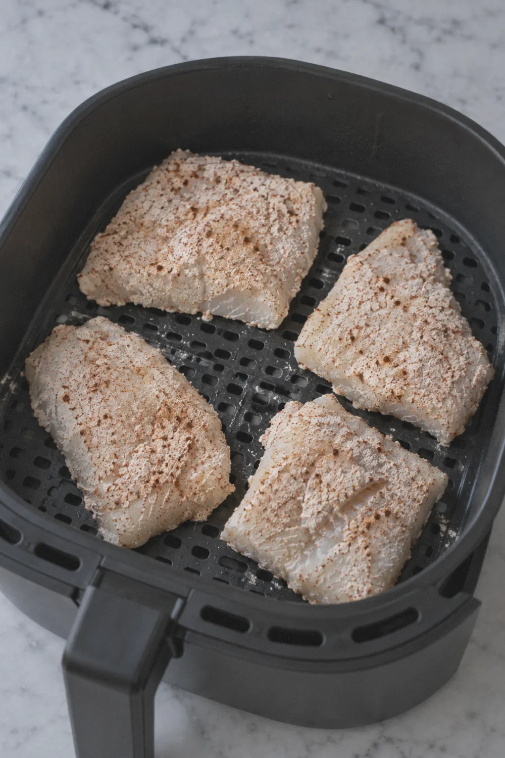 Seasoned cod fillets arranged in an air fryer basket
