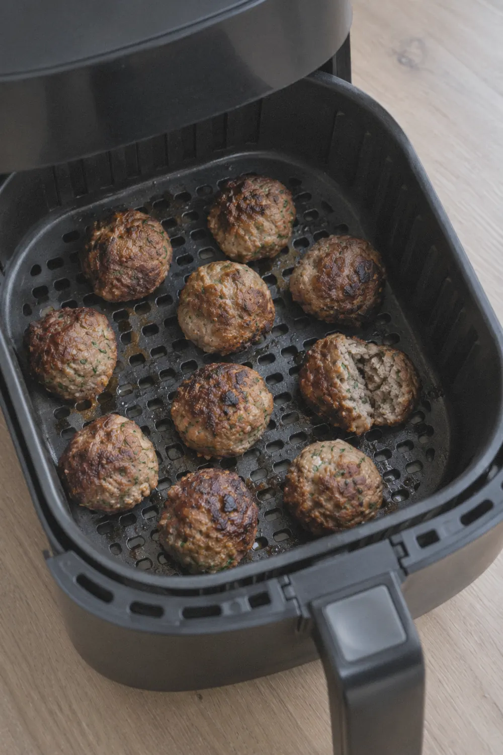 Browned meatballs arranged in a single layer inside an air fryer basket after cooking