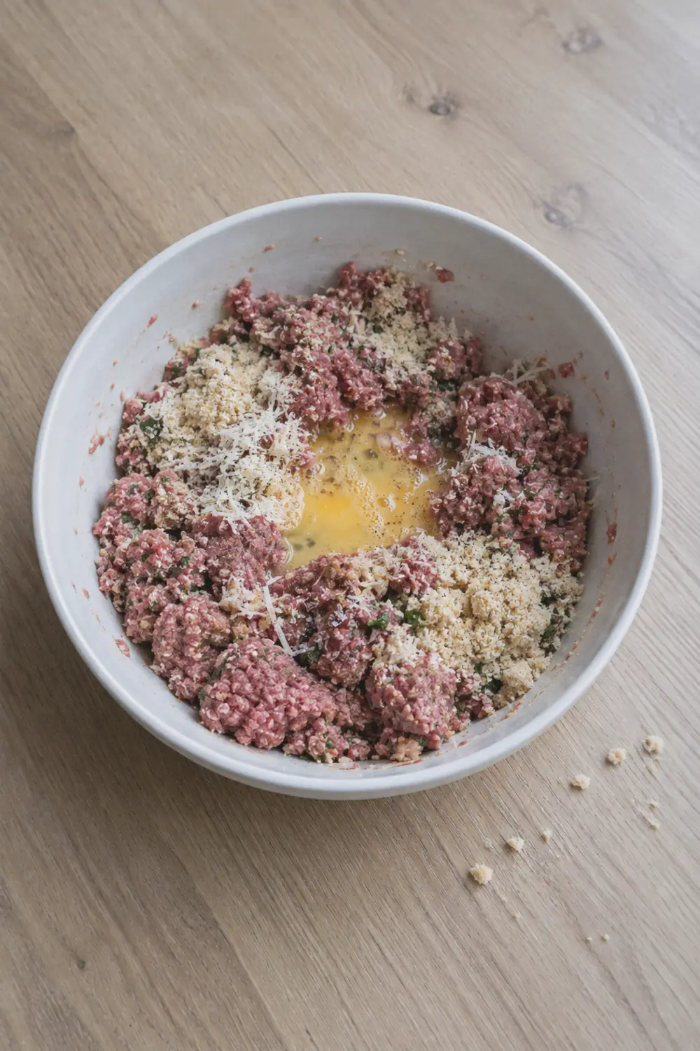 Raw meatball mixture in a large bowl with visible breadcrumb and Parmesan flecks throughout the ground beef