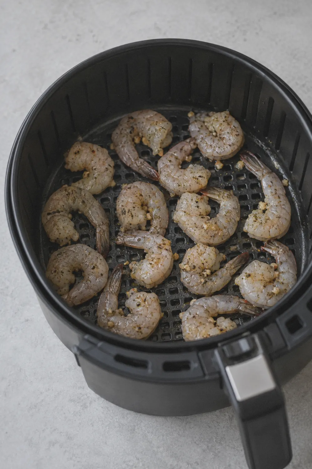 Shrimp arranged in a single layer inside the air fryer basket before cooking