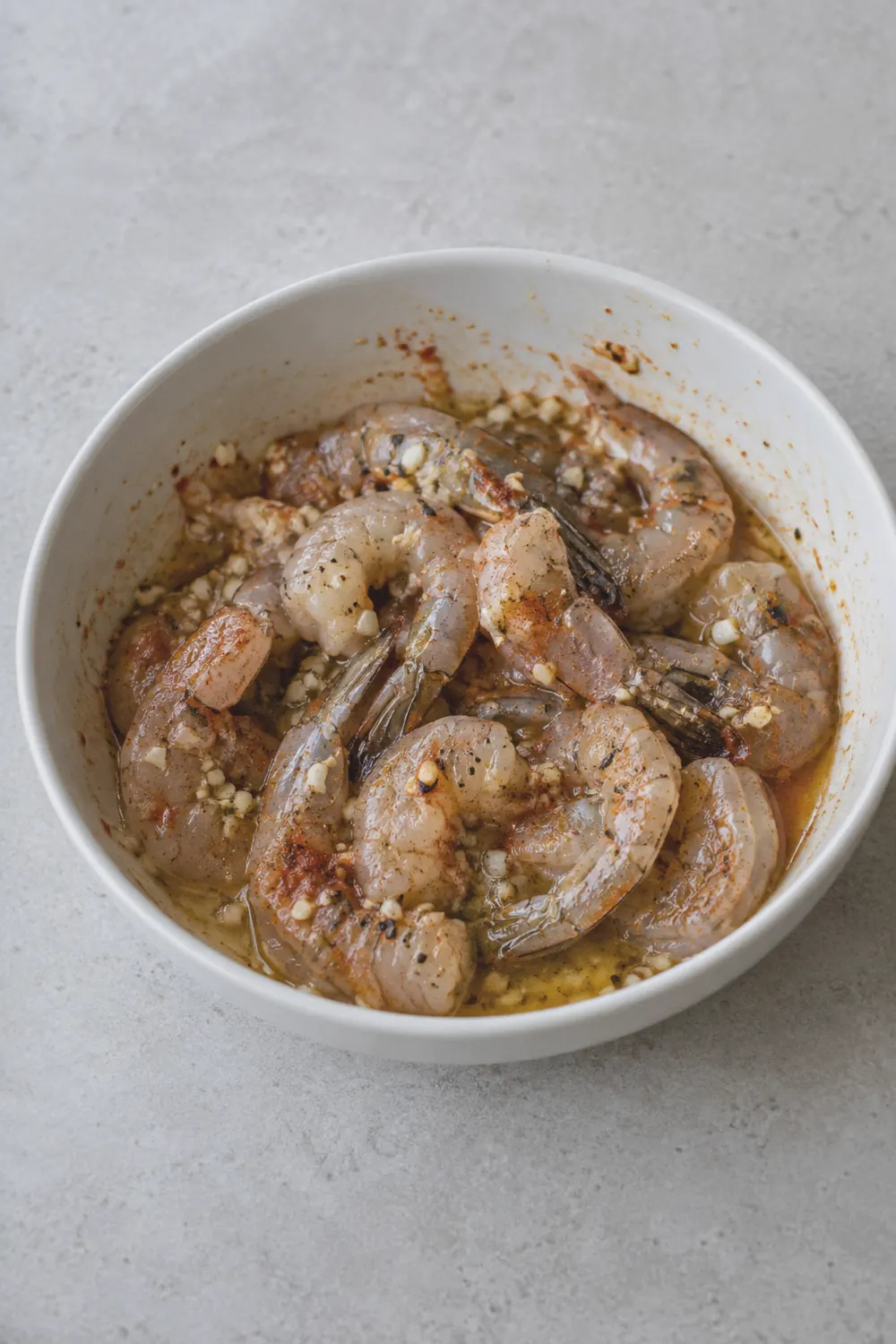 Raw seasoned shrimp tossed in garlic butter and spices in a bowl