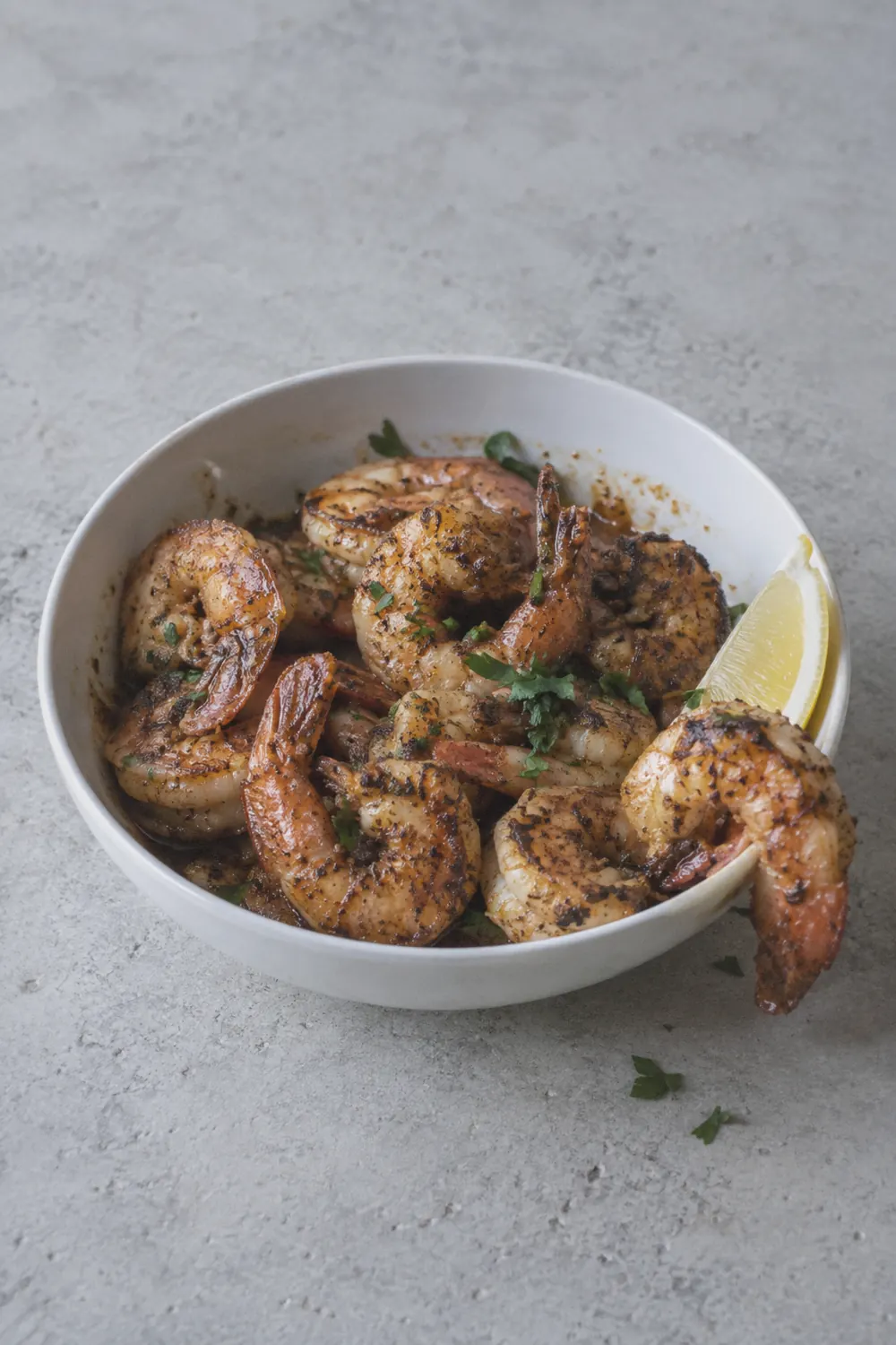 Seasoned air fryer shrimp with curled tails and lightly browned edges in a white bowl on a light surface