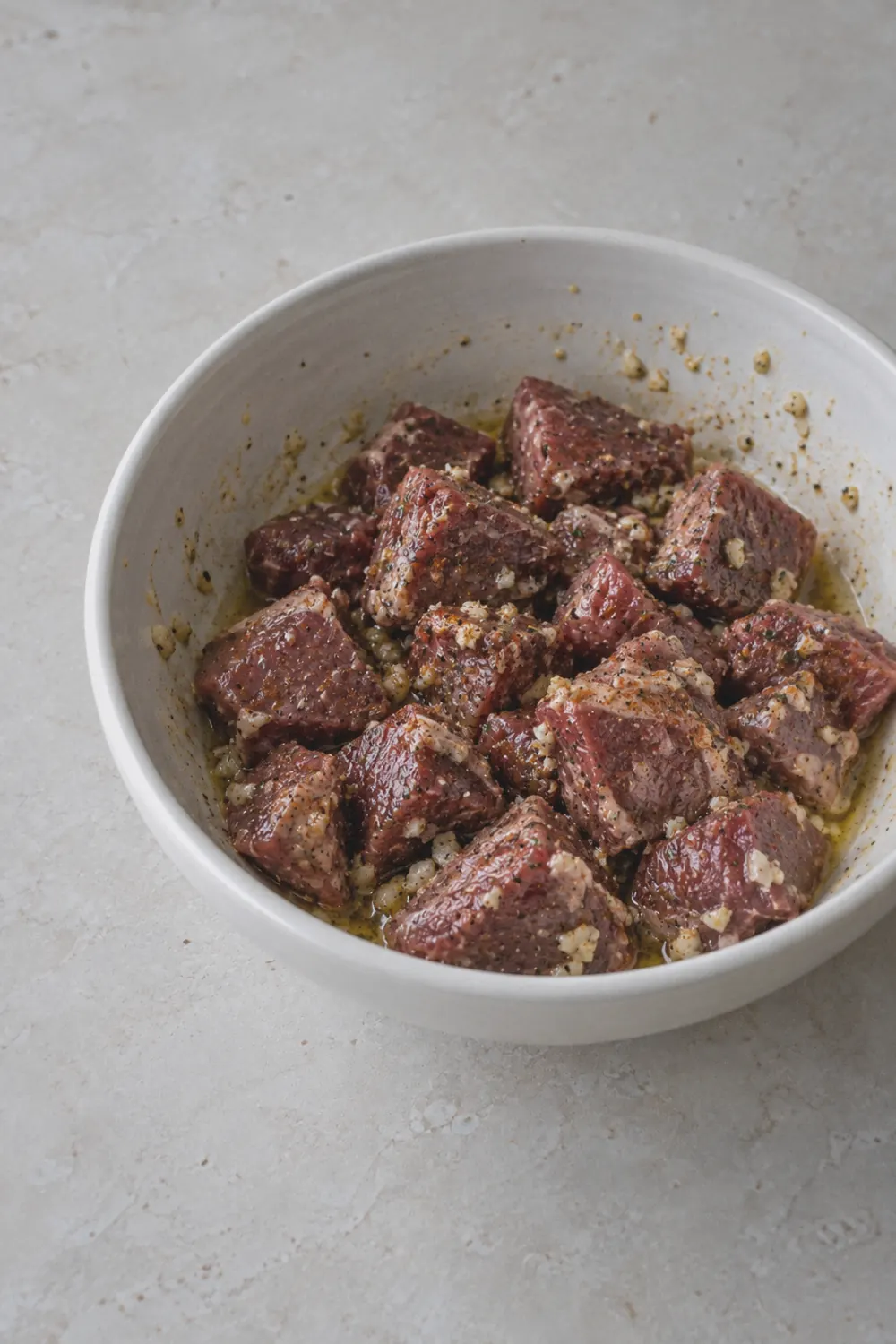 Raw seasoned steak cubes tossed in garlic butter and spices in a bowl