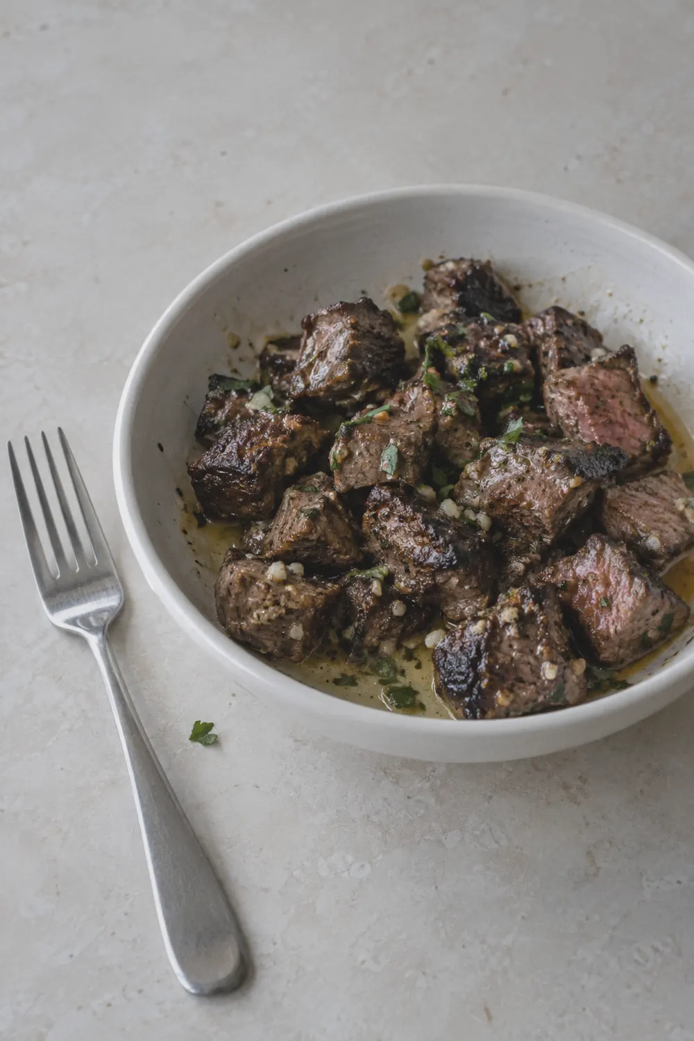 Seared steak bites with browned edges and garlic butter in a white bowl on a light surface