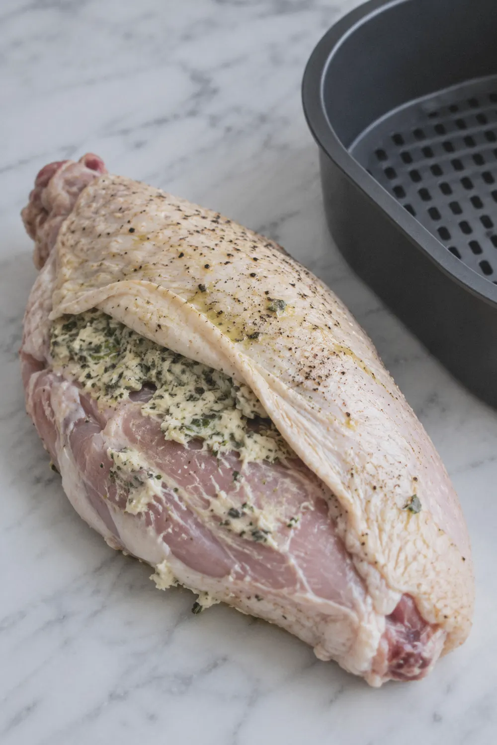 Raw turkey breast on a cutting board with herb butter being spread under the loosened skin