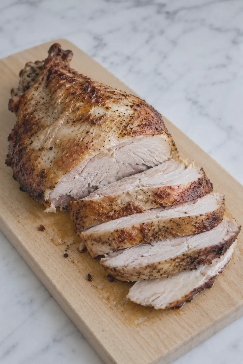 Golden brown air fryer turkey breast resting on a wooden cutting board with several slices cut showing juicy white meat inside