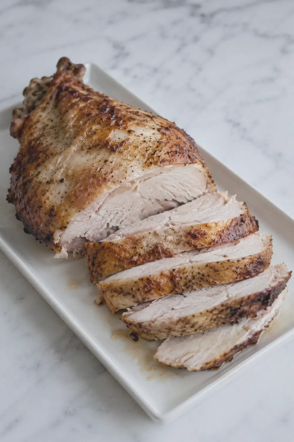 Sliced air fryer turkey breast with golden herb-seasoned skin on a white cutting board