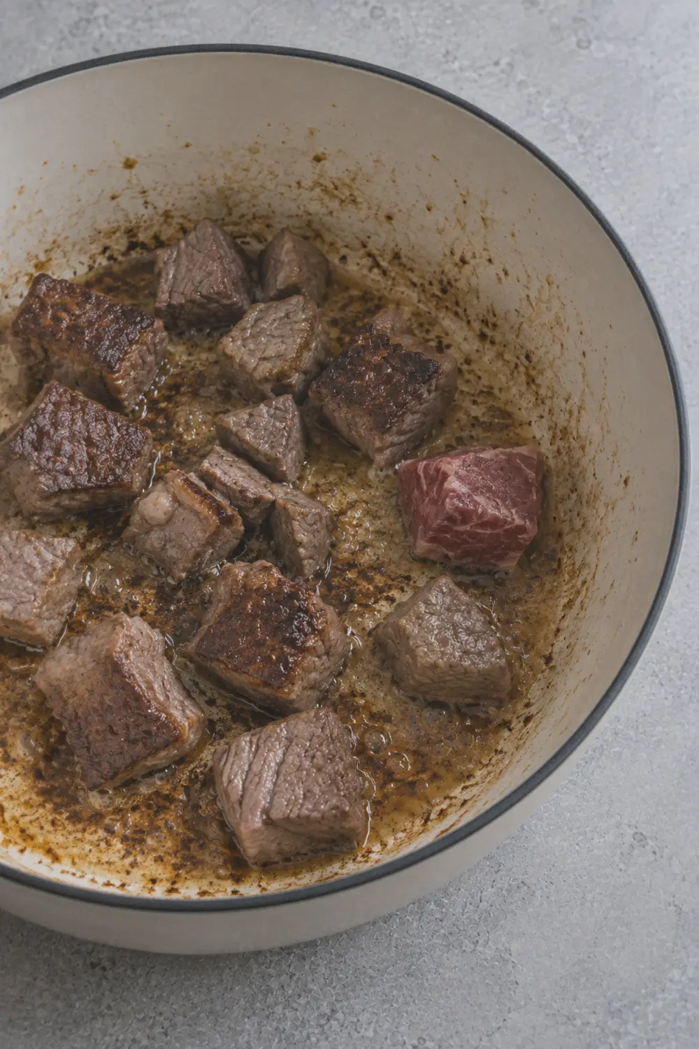 Cubes of beef chuck searing in a hot Dutch oven with deep brown crust forming on the bottom surface and golden fond developing on the pot