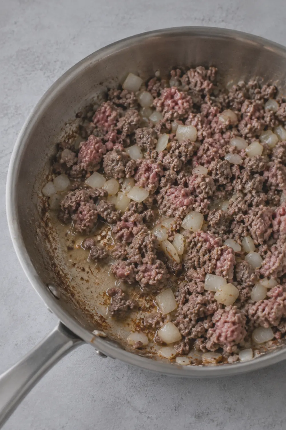 Browning seasoned ground beef with diced onion in a large skillet