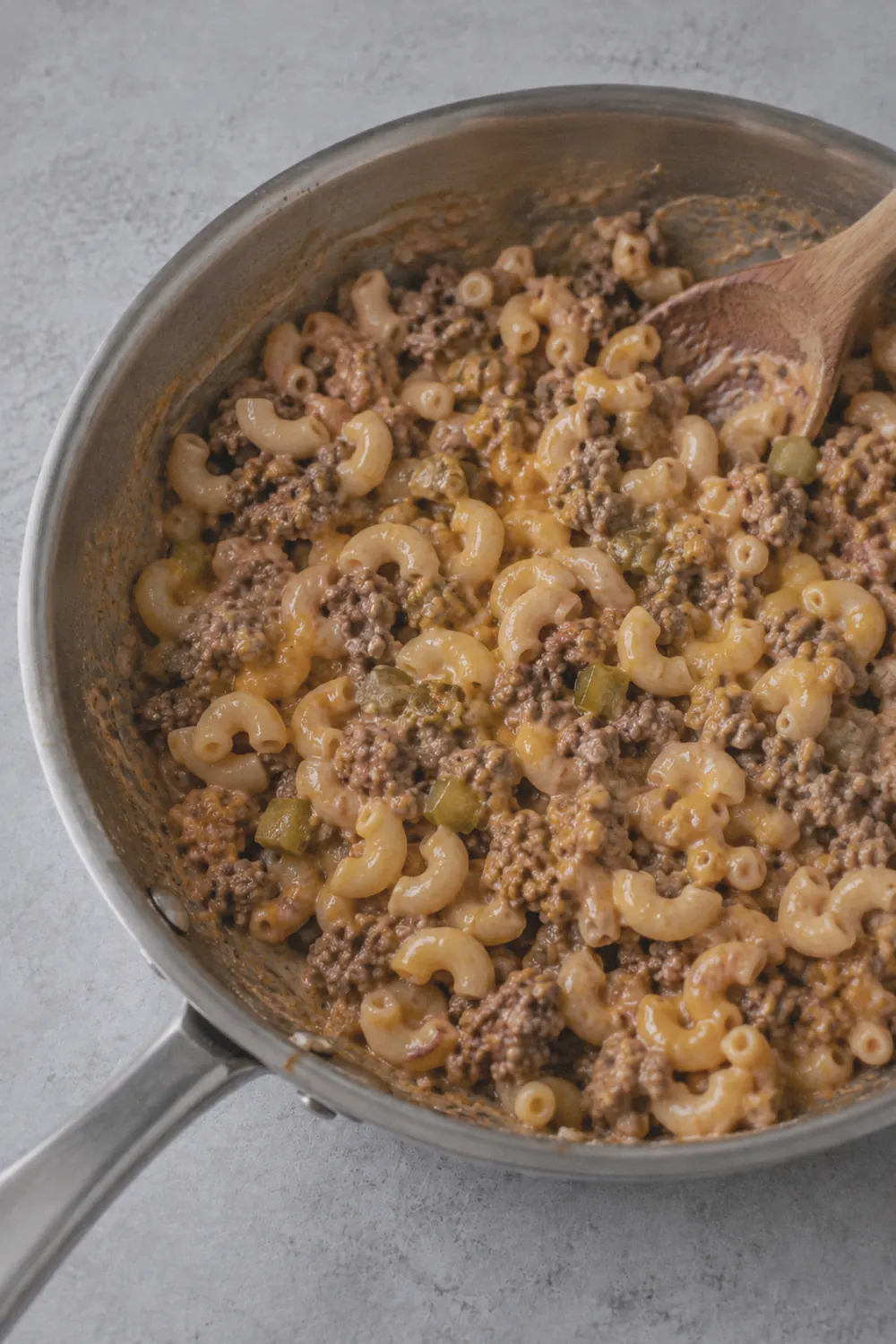 Elbow macaroni folded into the cheeseburger sauce with cheddar and chopped pickles in the skillet