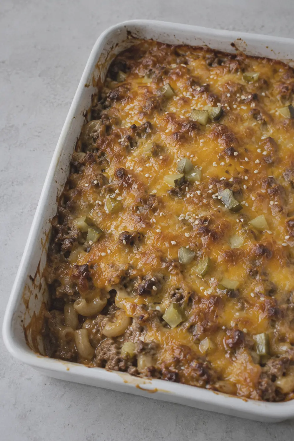 Cheeseburger casserole in a 9x13 baking dish with melted cheddar on top and diced pickles scattered over the cheese