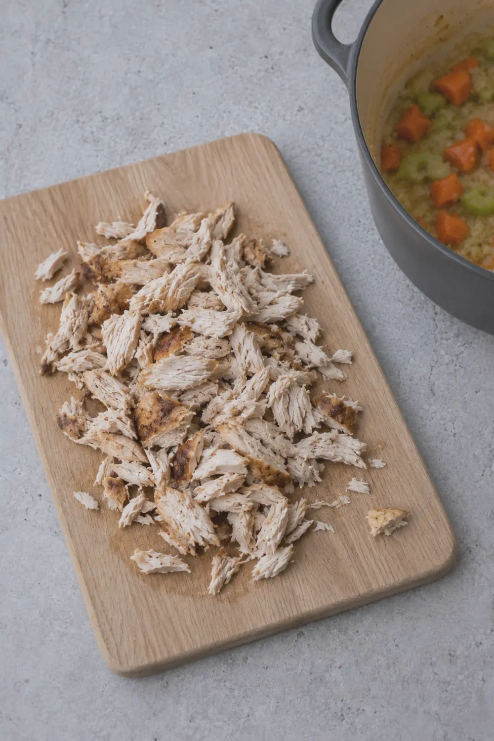 Shredded chicken on a cutting board next to the Dutch oven