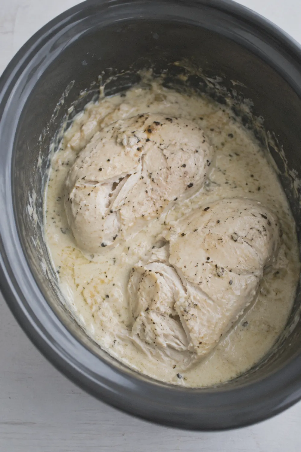 Cooked chicken breasts in thickened alfredo sauce inside the slow cooker