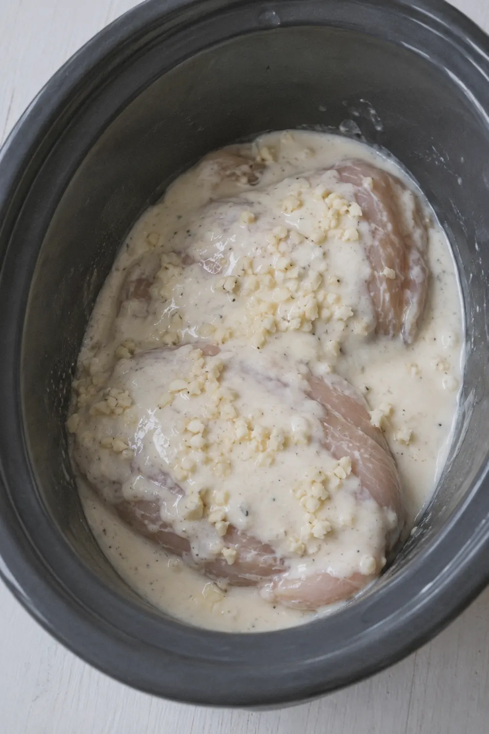 Seasoned chicken breasts with alfredo sauce poured over them in a slow cooker