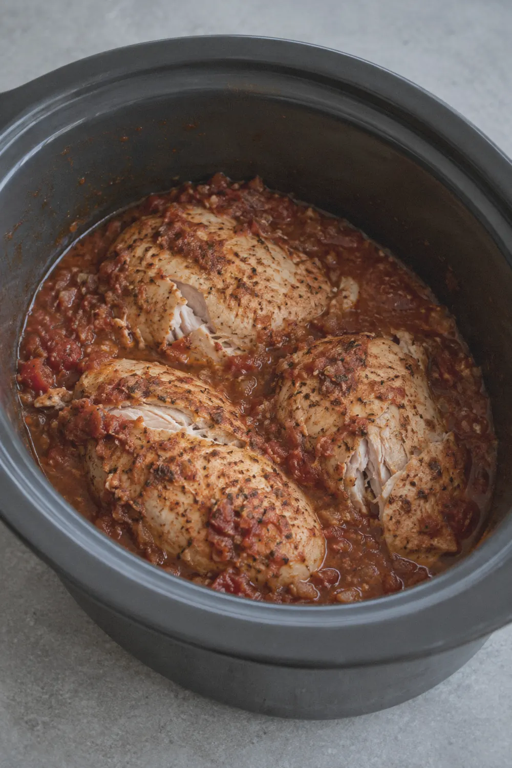 Seasoned chicken breasts in a slow cooker insert covered with chunky salsa and lime juice before cooking, viewed from above at an angle