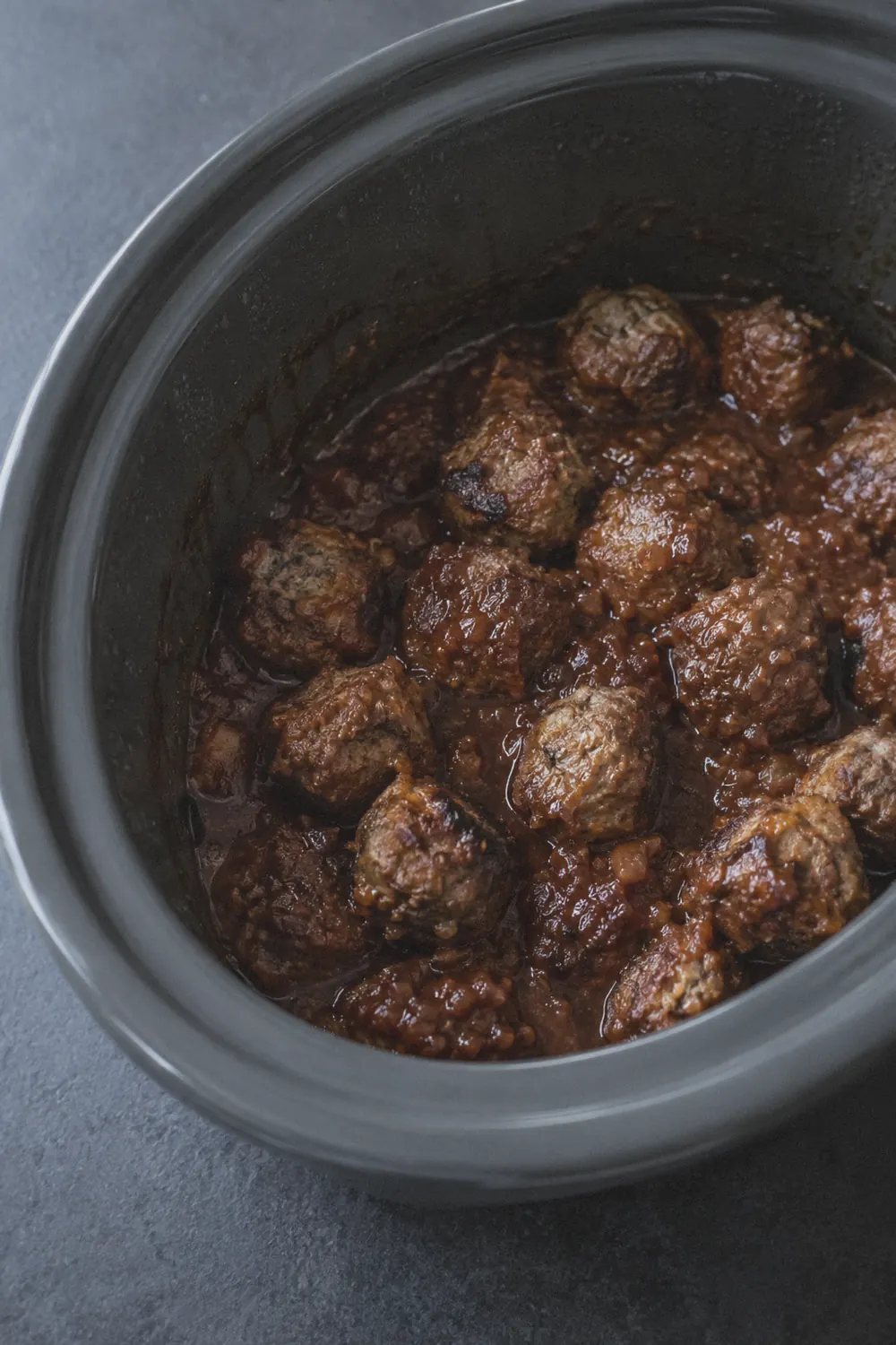 Meatballs halfway through cooking in the slow cooker, sauce thickened and clinging