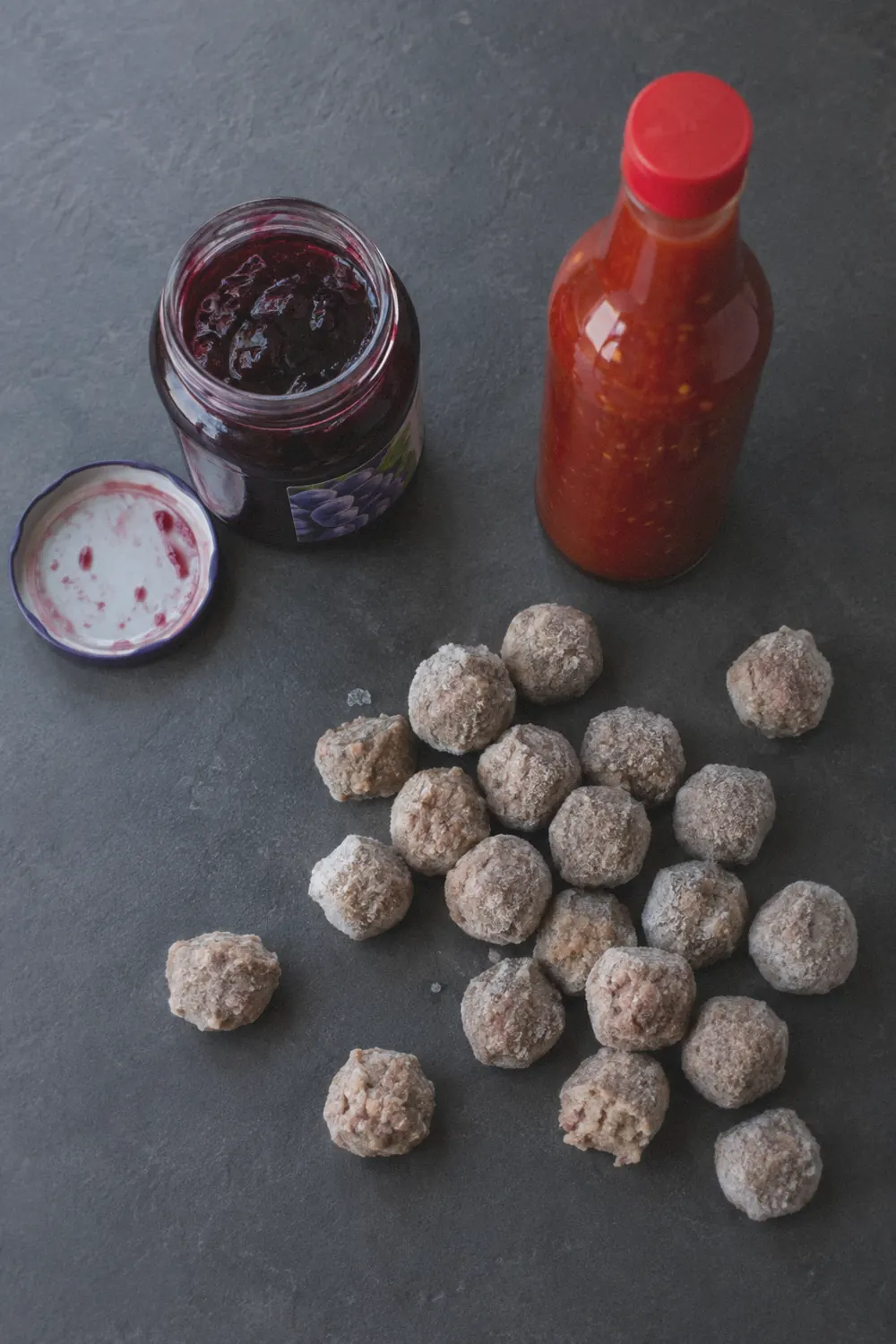 Ingredients for grape jelly meatballs laid out on a dark slate surface
