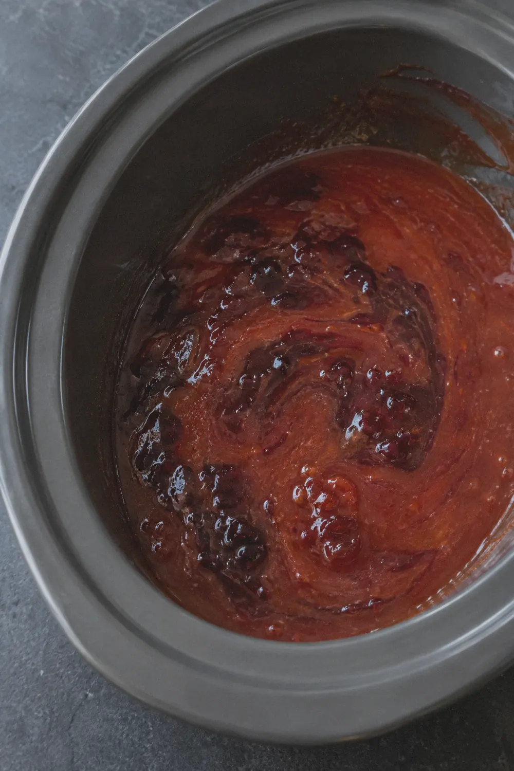 Grape jelly and chili sauce being stirred together in a slow cooker insert