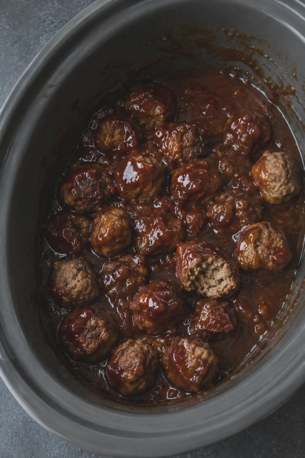 Crockpot grape jelly meatballs in a dark slate slow cooker insert, coated in glossy sweet chili sauce