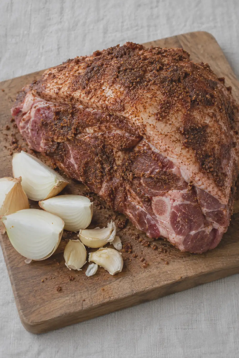 Seasoned raw pork shoulder with a dark spice rub sitting in a slow cooker insert with quartered onions visible underneath