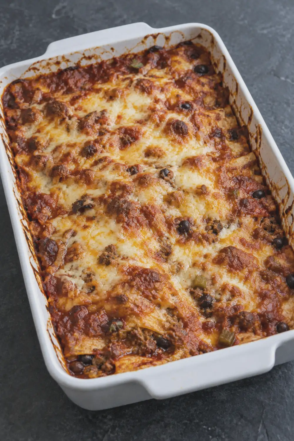 Baked enchilada casserole fresh from the oven with melted browned cheese and visible bubbling sauce at the edges