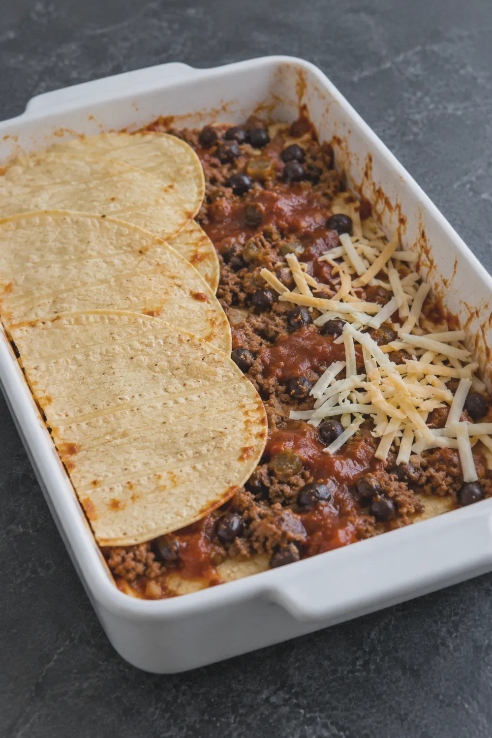 Layering corn tortillas over enchilada sauce and beef in a 9x13 baking dish