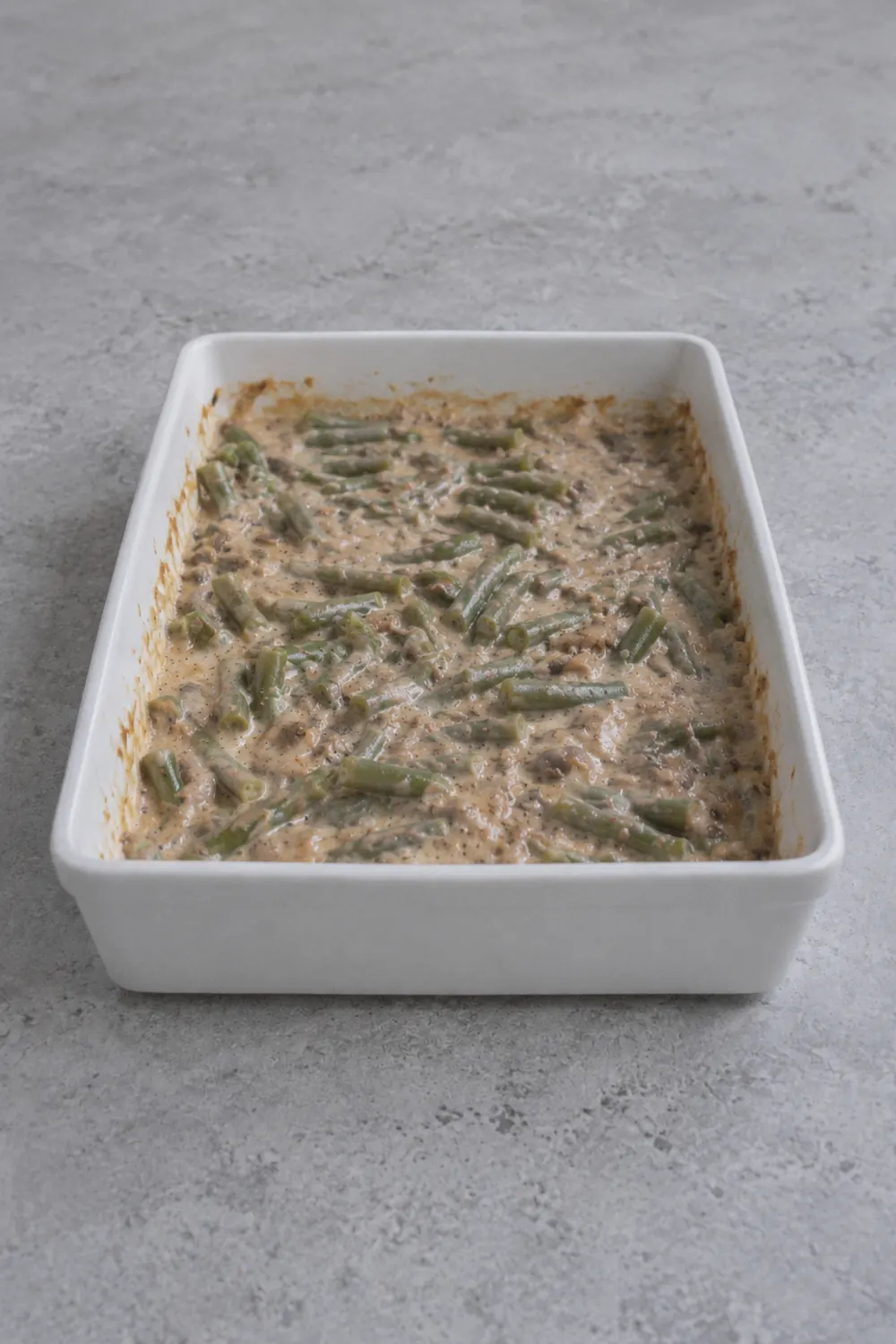 Creamy green bean mixture in a white baking dish ready to go in the oven