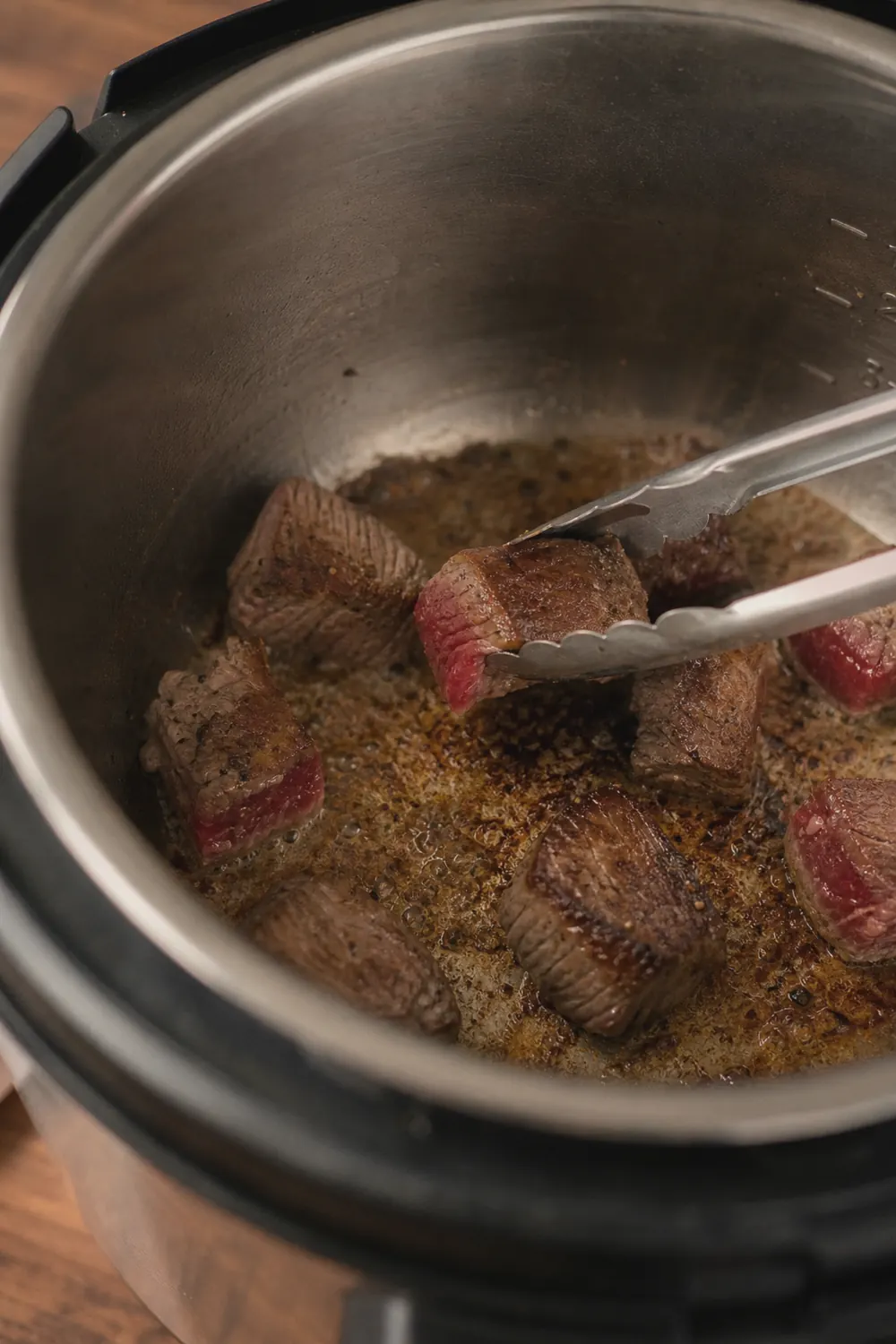 Beef cubes browning in the Instant Pot on sauté mode, golden crust forming on the surface