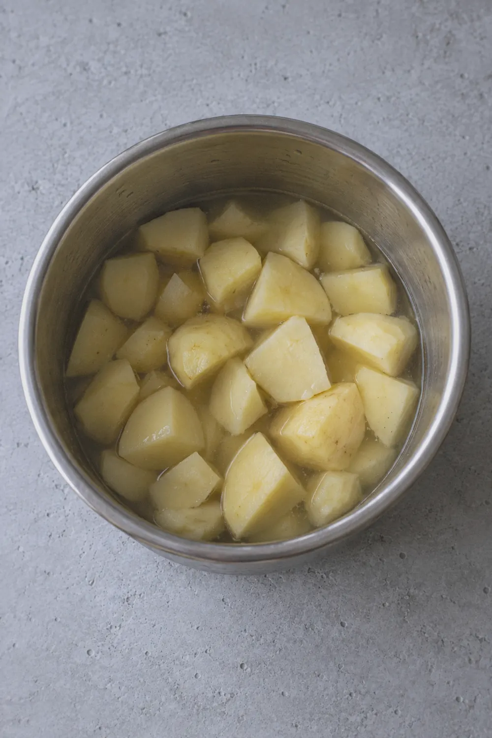 Peeled Yukon Gold potato chunks arranged in the Instant Pot inner pot with water, some pieces slightly larger and more irregular than others, viewed from directly above