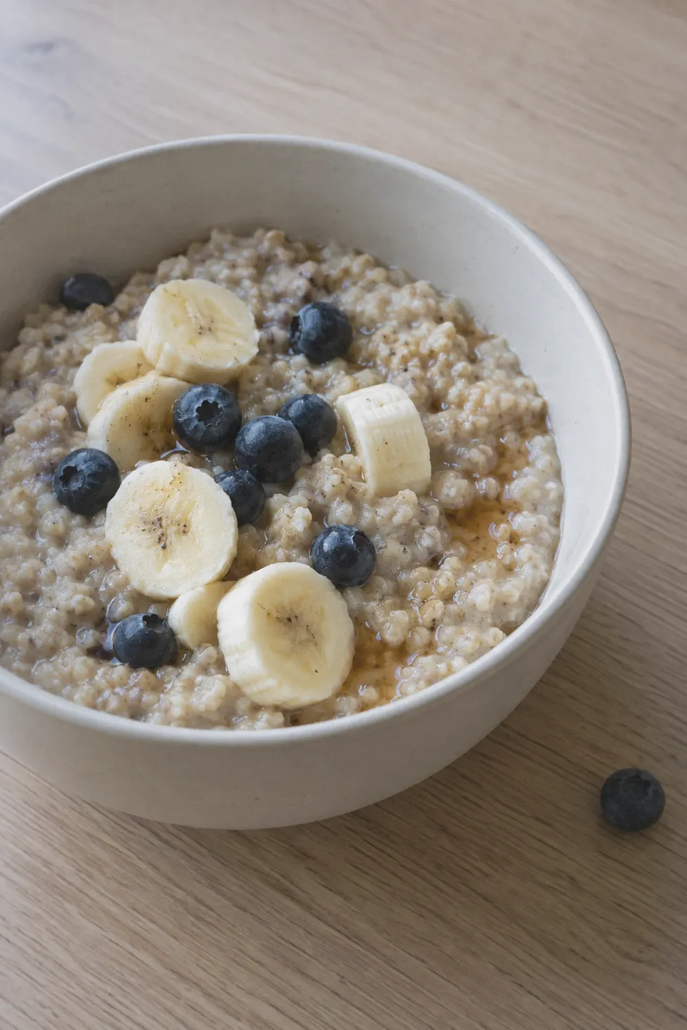 Bowl of creamy steel-cut oatmeal made in the Instant Pot topped with sliced banana and fresh blueberries on a pale oak surface