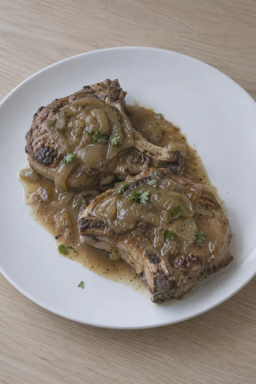 Finished Instant Pot pork chops on a white plate with thick brown onion gravy pooled around and over the chops, a few pieces of softened onion visible in the gravy, garnished with chopped parsley