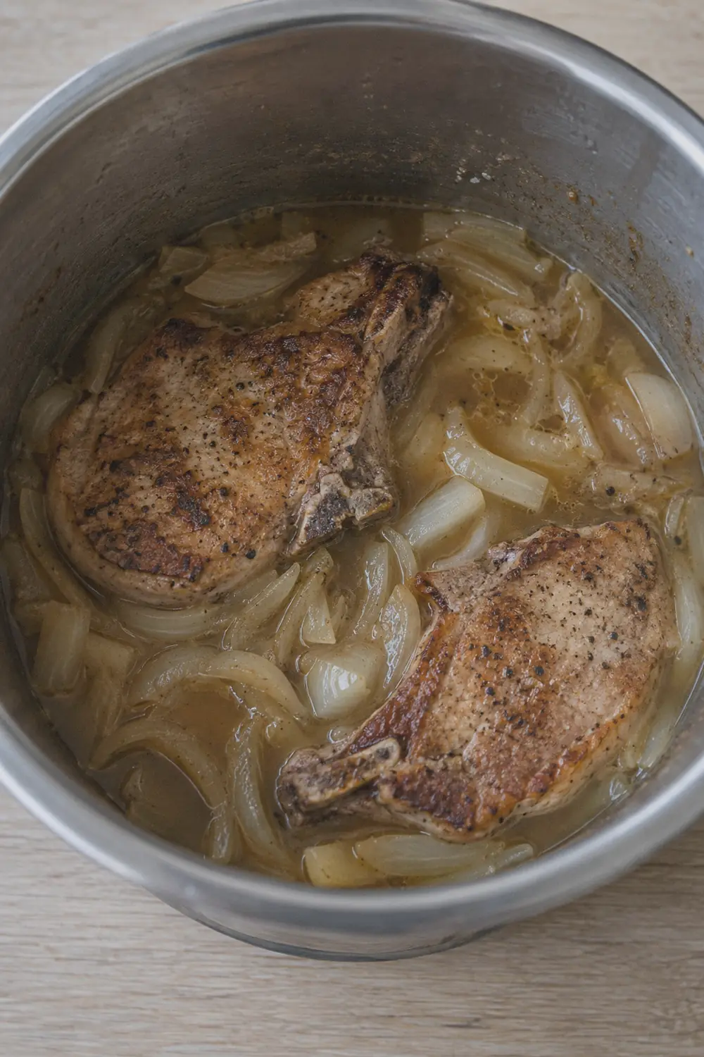Pork chops nestled into the Instant Pot inner pot surrounded by sliced onions and light brown broth, viewed from above before the lid goes on