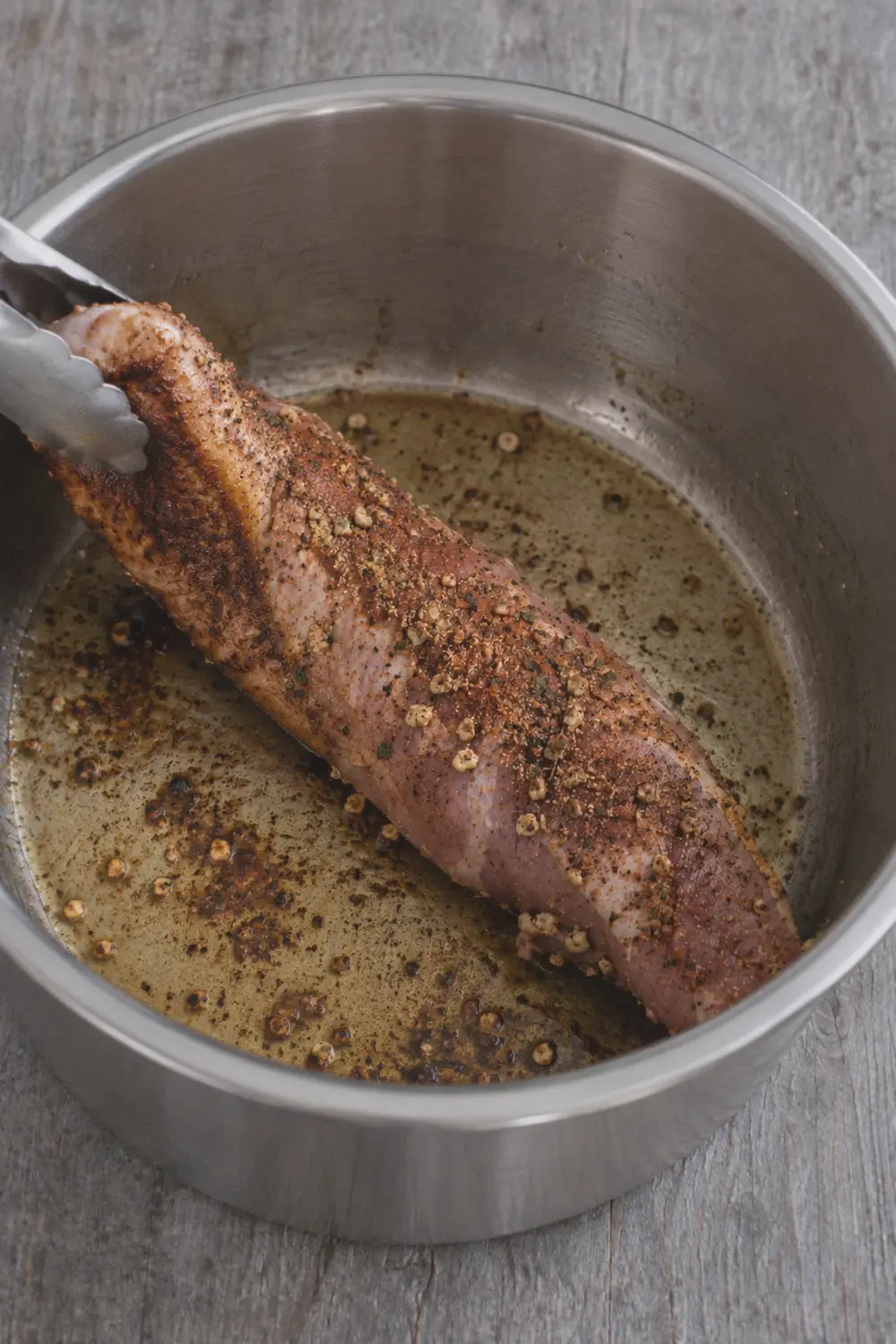Pork tenderloin searing in the Instant Pot inner pot with a deep brown crust forming on one side, tongs holding one end slightly lifted to show the browning underneath