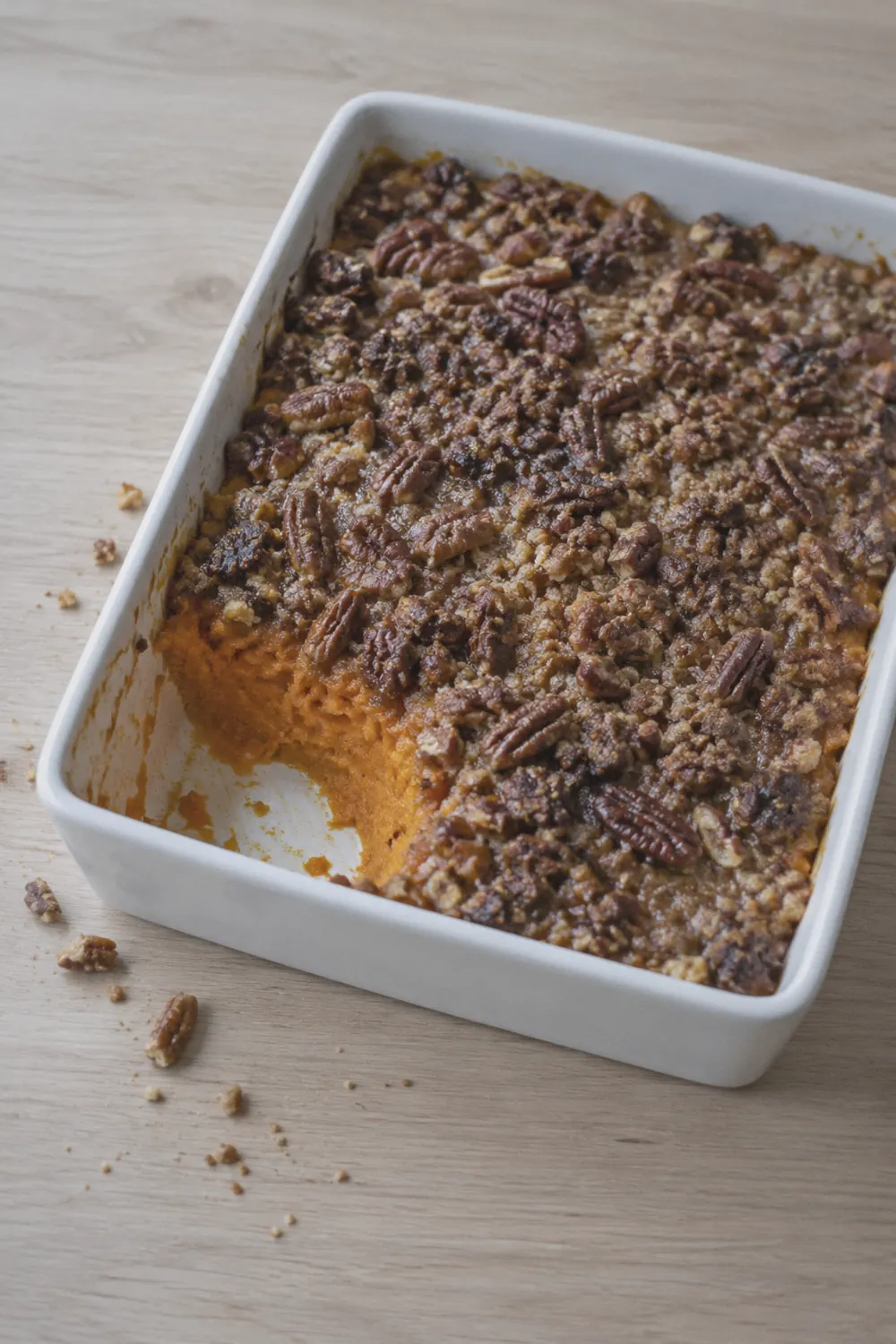 Sweet potato casserole with pecan streusel topping in a white ceramic baking dish on a pale oak surface