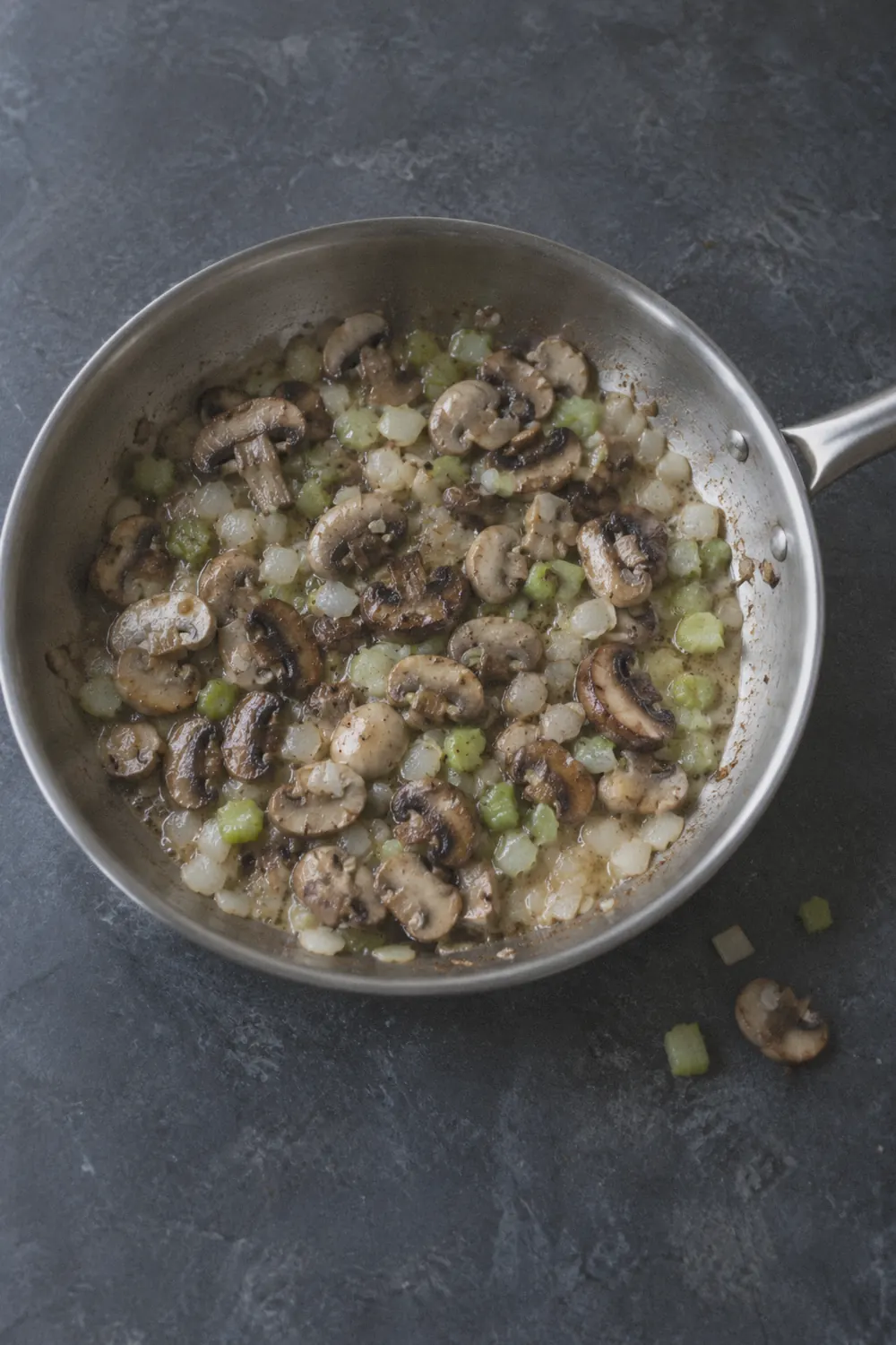 Sliced cremini mushrooms cooking with diced onion and celery in a large skillet